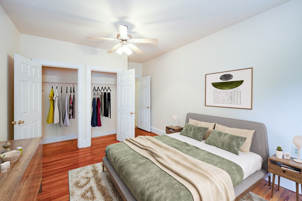 A bedroom with a bed, a ceiling fan, and a wardrobe with clothes hanging.