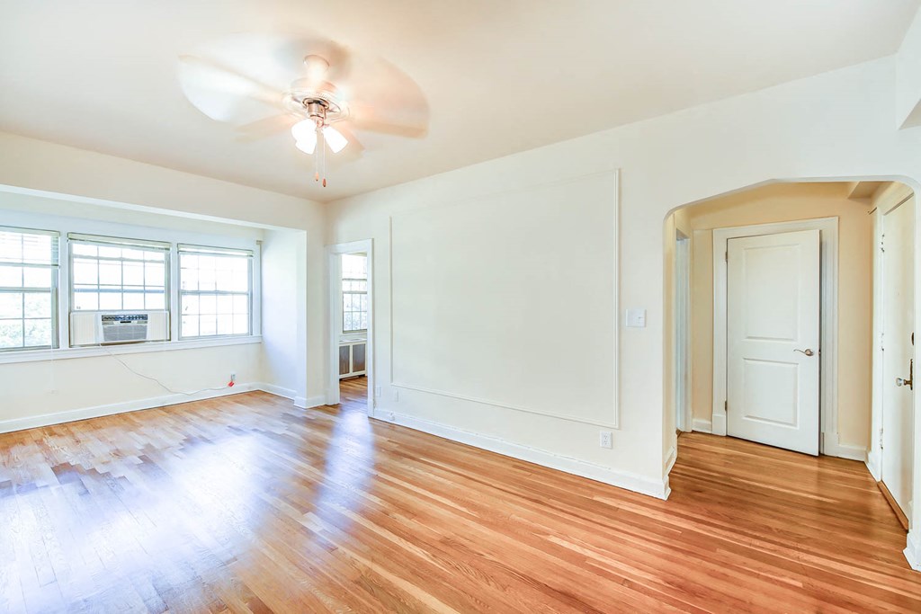 vacant living area with hardwood floors, ceiling fan, large windows and view of front entrance