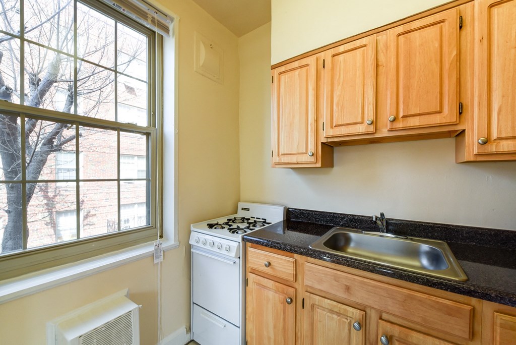 kitchen with gas range, wood cabinetry and large window at 1401 sheridan apartments in washington dc