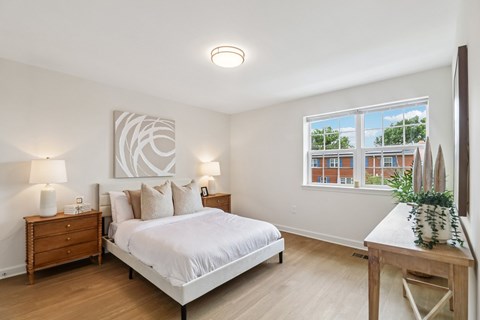 A bedroom with a large bed, a nightstand with a lamp, and a wooden table with a plant on it.