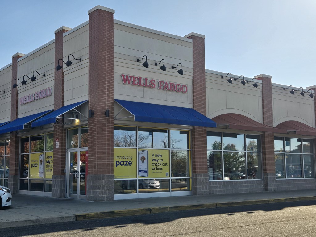 A Wells Fargo bank with a blue awning and a white car parked in front.