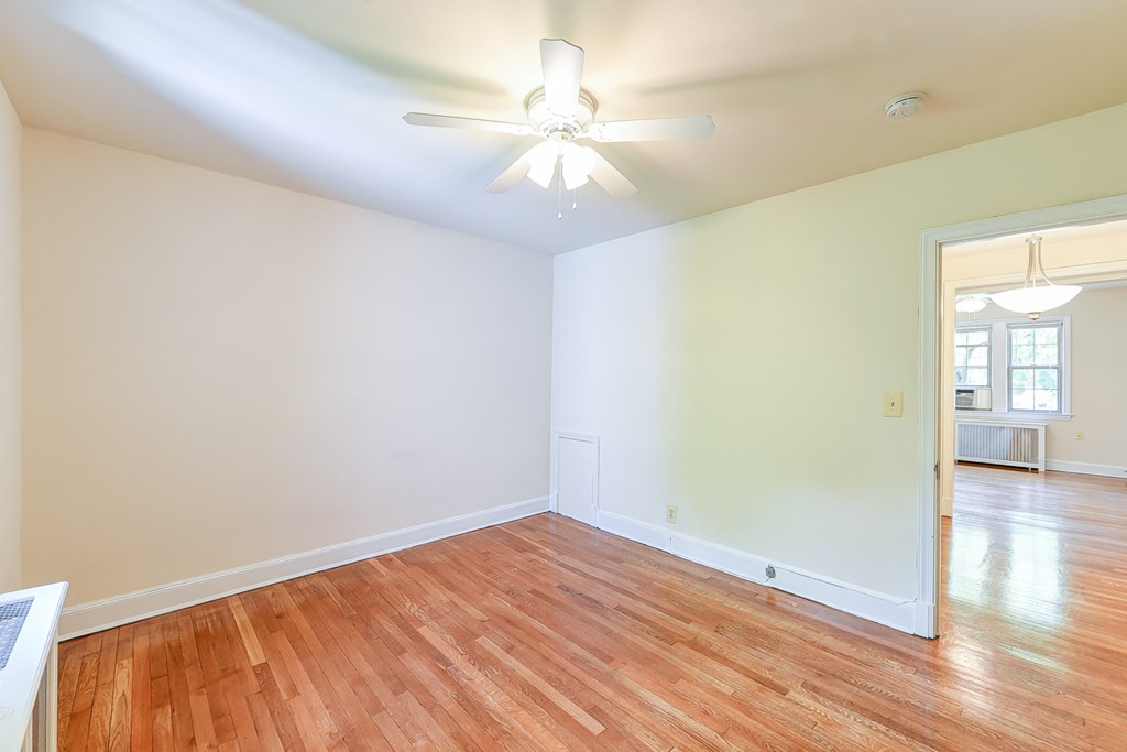 vacant bedroom with hardwood flooring, ceiling fan and view of living area  at  2629 39th Street apartments in washington dc