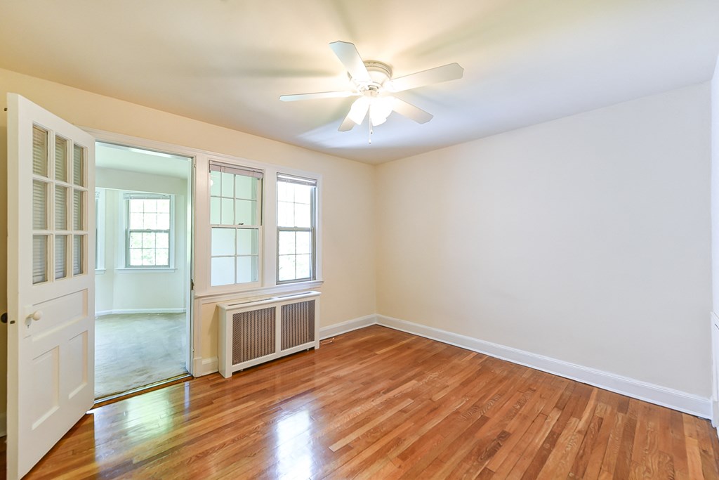 vacant bedroom with hardwood floors, ceiling fan, and doorway to sunroom den  at  2629 39th Street apartments in washington dc