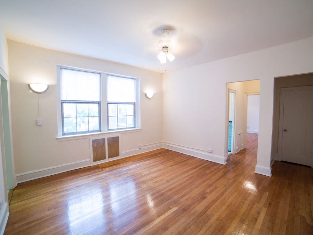 vacant living area with hardwood floors, large windows and ceiling fan at 2800 ontario road apartments in washington dc