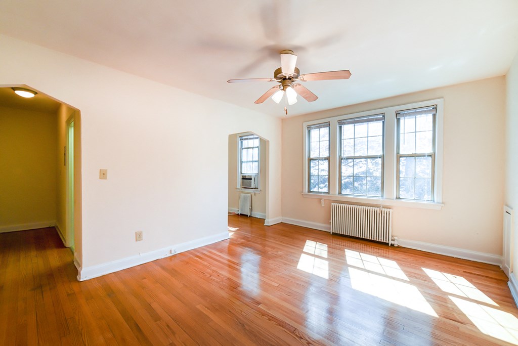 vacant living area with hardwood flooring, ceiling fan and large windows at 3101 Pennsylvania apartments in washington dc