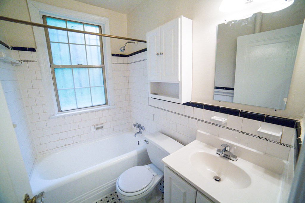 bathroom with cabinet, tub, toilet, vanity, large mirror and window at 3101 pennsylvania apartments in washington dc