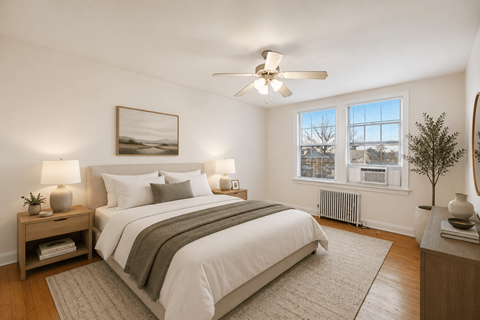 A bedroom with a large bed, a ceiling fan, and a window with a view of a cityscape.