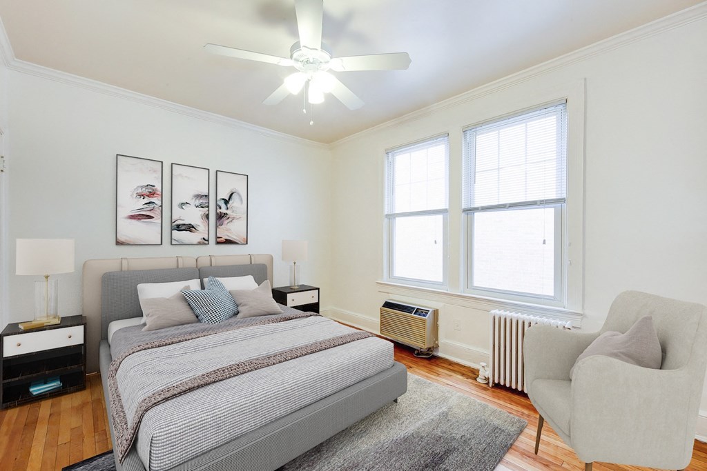 bedroom with bed, nightstands, sitting area, large windows and ceiling fan at 3213 wisconsin apartments in washington dc