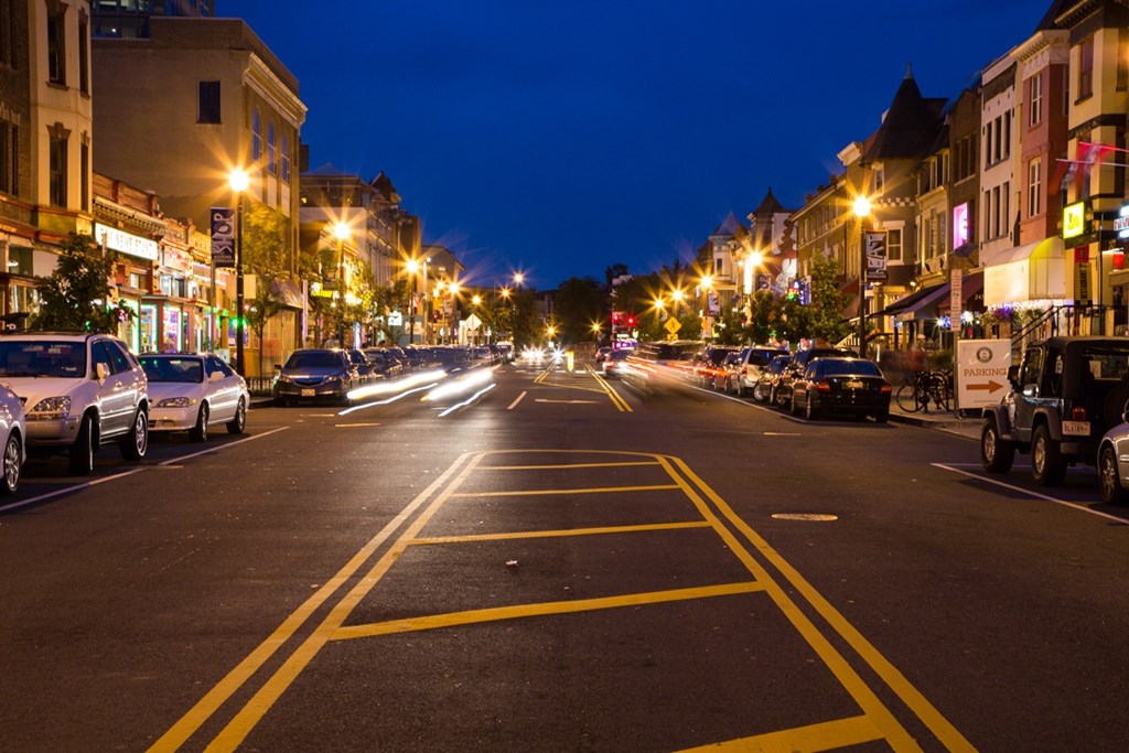 A city street at night with cars parked on the side.