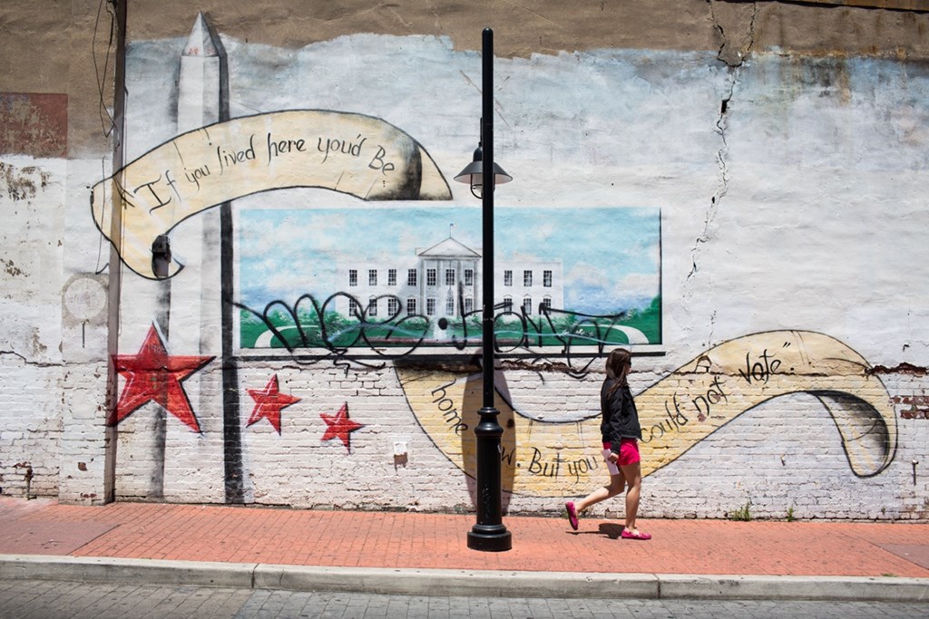A woman walks past a mural of a white house with a banner that reads "If you find here you're lost".