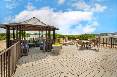 A wooden gazebo is surrounded by chairs and tables on a deck.