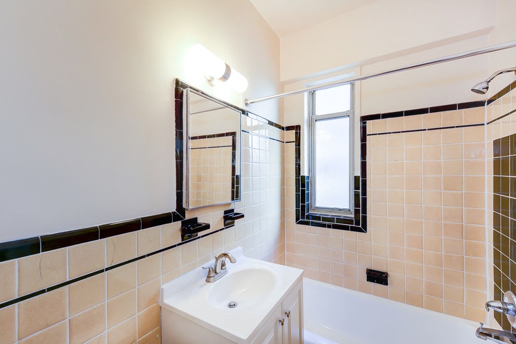 bathroom with tub, vanity, large mirror, tile details and window at baystate apartments in washington dc