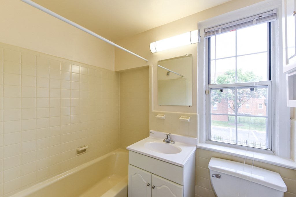 bathroom with vanity, mirror, tub, toilet and window at colonnade apartments in washington dc
