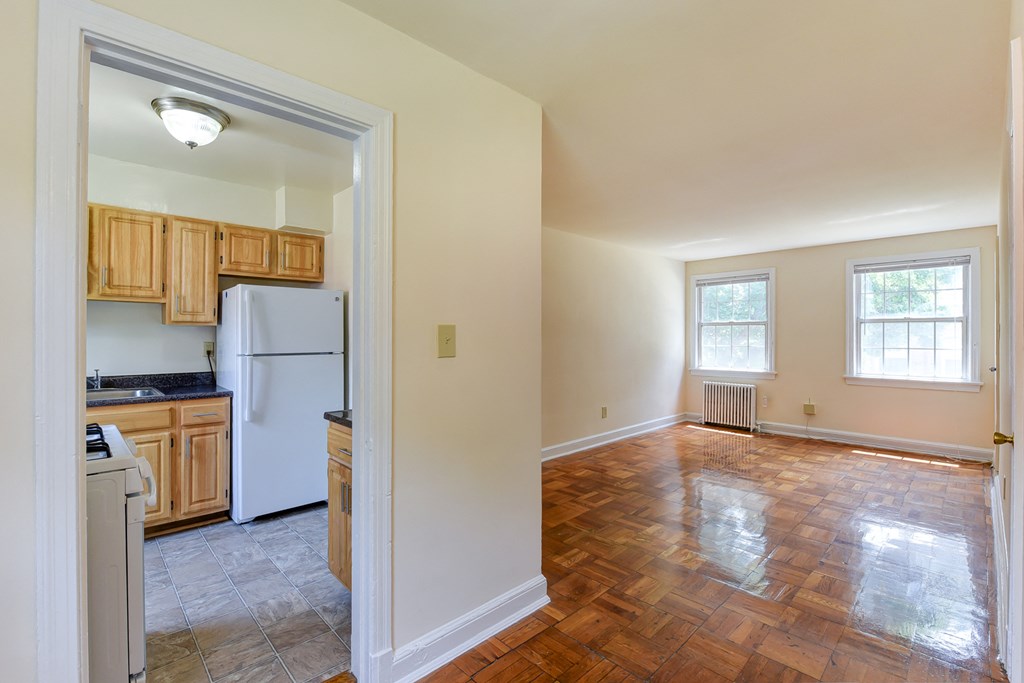vacant living area with hardwood flooring, large windows and view of kitchen at colonnade apartments in washington dc