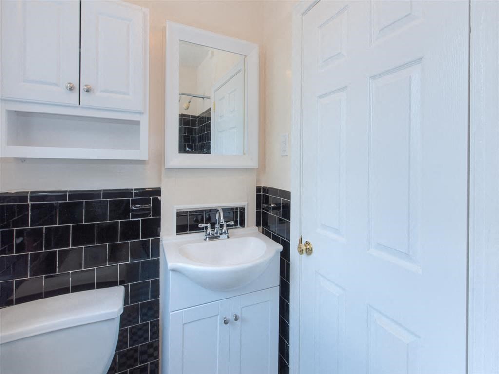 bathroom with toilet, sink, cabinetry and mirror at 6100 14th Street apartments in washington dc