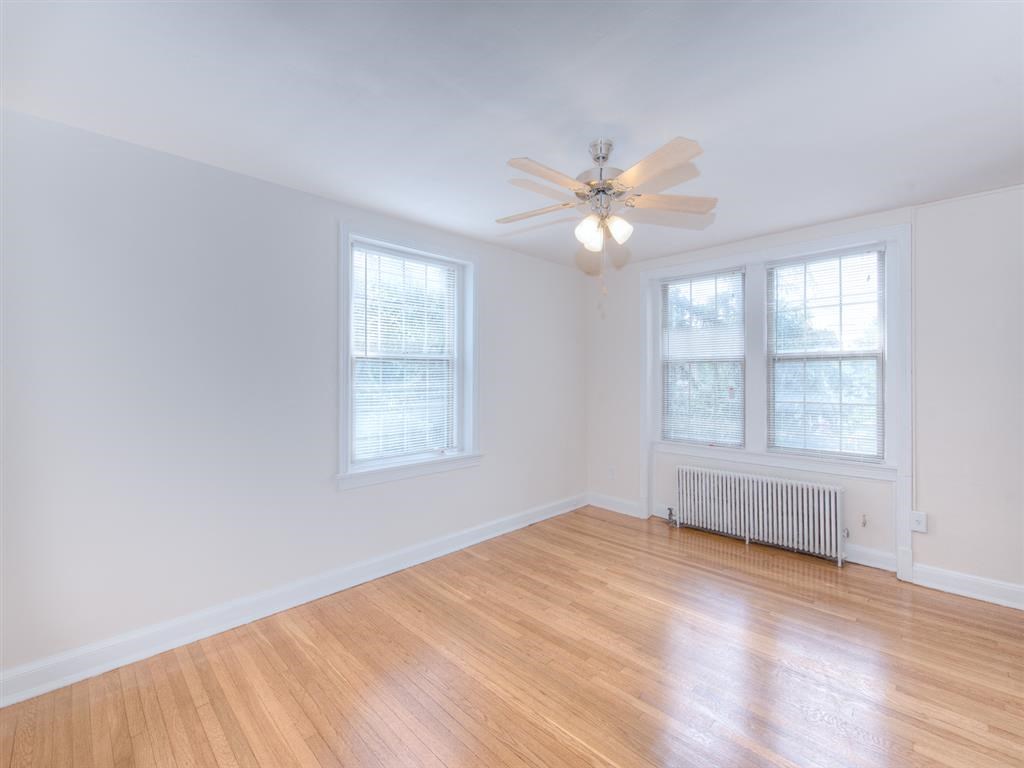 vacant living area with hardwood flooring, ceiling fan, and large windows at 6100 14th Street apartments in washington dc