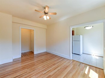 vacant living area with hardwood flooring, ceiling fan and view of kitchen at the klingle apartments in washignton dc - Photo Gallery 13