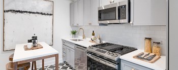 kitchen with white cabinetry, stainless steel appliances, microwave and kitchen island at the dahlia apartments in washington dc - Photo Gallery 3