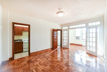 vacant living area with large windows, hard wood flooring and  view of kitchen and sunroom at eddystone apartments in washington dc - Photo Gallery 7