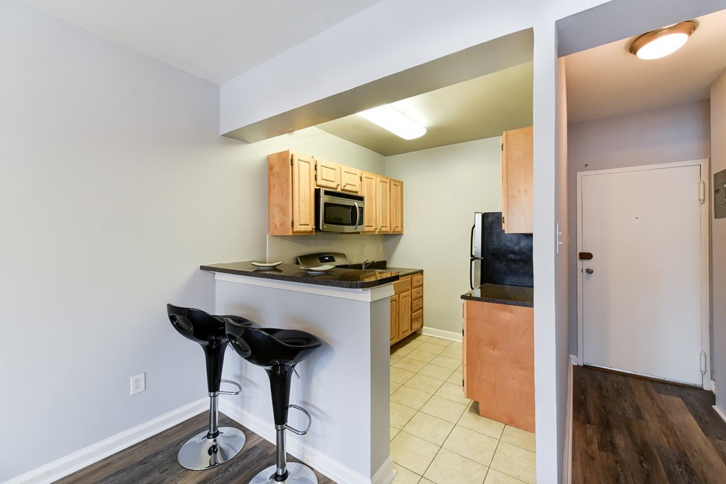 A kitchen with a bar stool and a microwave above the bar.