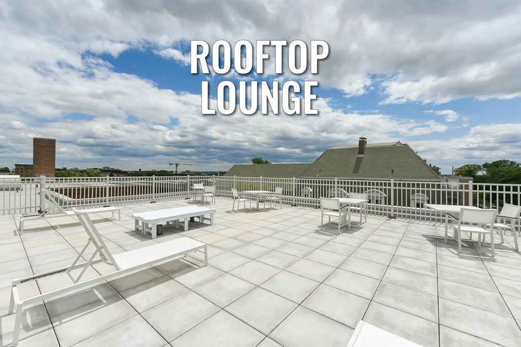A rooftop lounge with white furniture and a blue sky in the background.