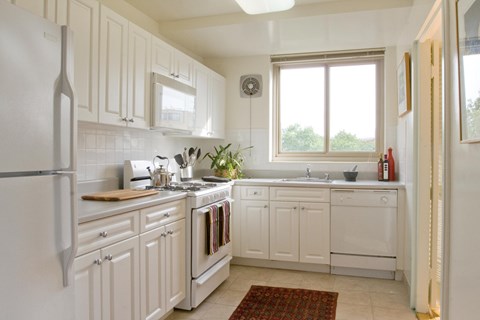 A white kitchen with a refrigerator on the left and a window above the sink.