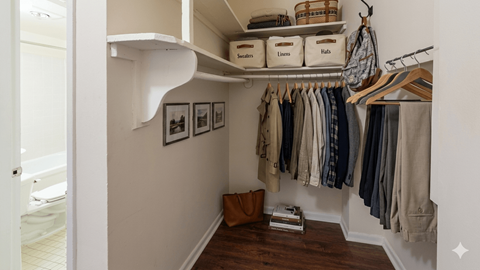 A small closet with clothes hanging and baskets on the shelf.