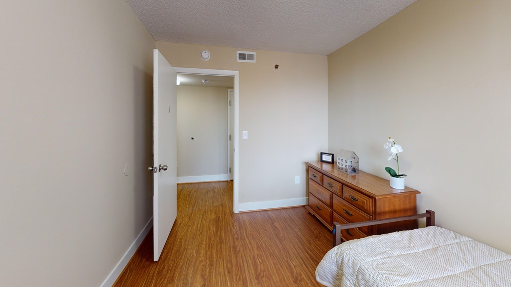 A bedroom with a bed, dresser, and open door leading to another room.