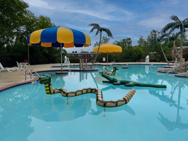 A pool with a blue and yellow umbrella and a green inflatable.