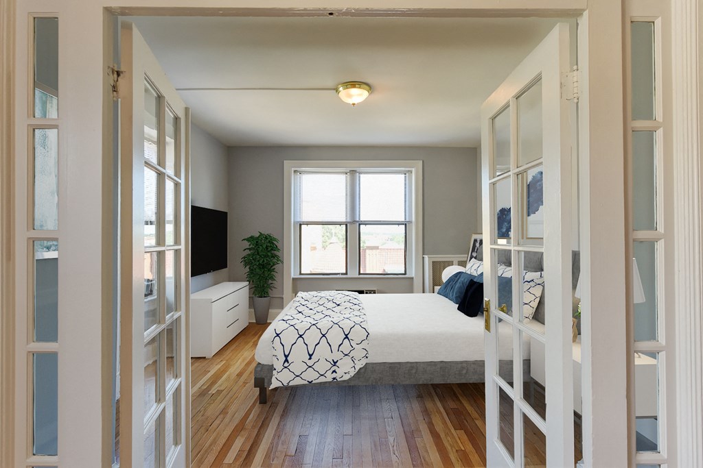 bedroom with bed, dresser, tv, hardwood flooring and large windows at the shawmut apartments in washington dc