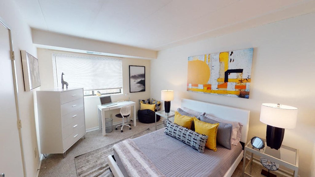 Bedroom with dresser, desk, bed, night stands, and large windows at washington view apartments in southeast dc