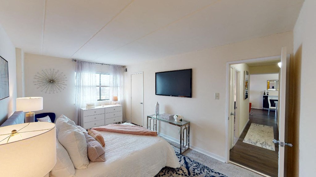 Bedroom with dresser, tv, bed and large windows at washington view apartments in southeast dc