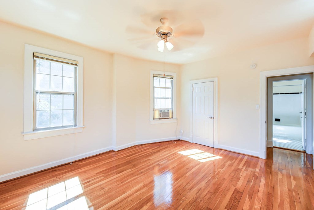vacant bedroom with hardwood floors, ceiling fan, large windows and view of bathroom at the frontenac apartments in van ness washington dc