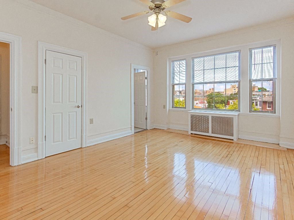 an empty living room with a ceiling fan, hardwood floors and three windows at the calverton apartments in washington dc