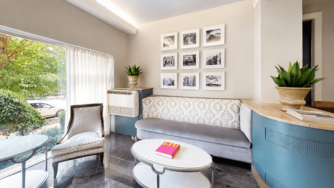 A living room with a grey couch, a white coffee table, and a glass table with a plant on it.