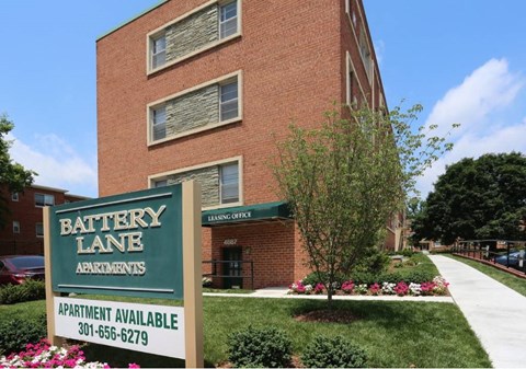 A sign for Battery Lane Apartments is in front of a brick building.