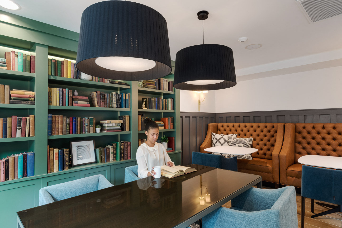 A woman is sitting at a table in a room with a bookshelf behind her.