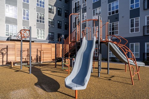 A playground with a slide and climbing structures in front of a building.