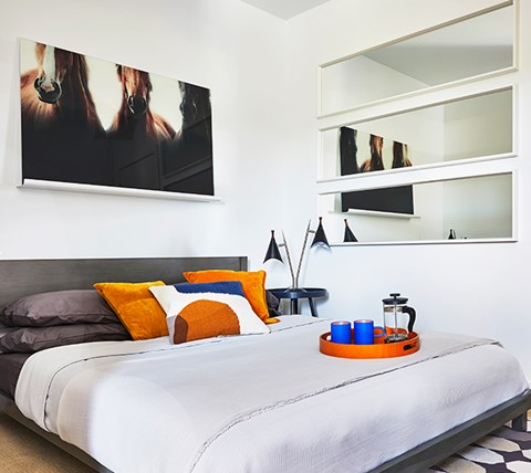 A bed with a grey headboard and a white comforter with orange and blue pillows.