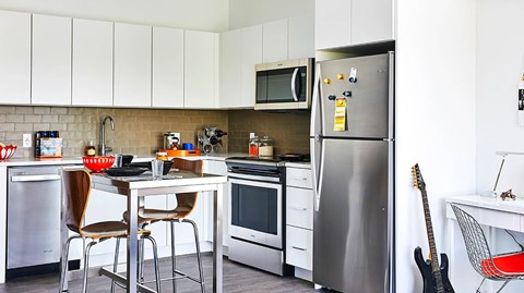 A kitchen with a refrigerator, oven, and a dining table with chairs.