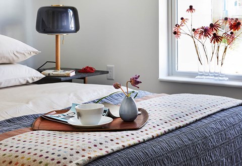A tray with a cup and a vase on it is on a bed.