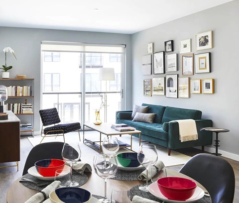 A living room with a green couch, a dining table with chairs, and a bookshelf.