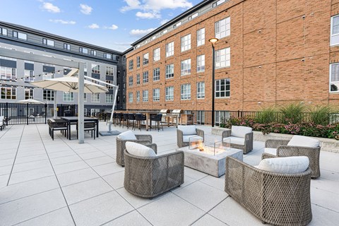 A patio with a fire pit and wicker chairs.