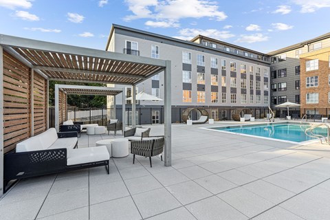 A pool area with a wooden pergola and white furniture.