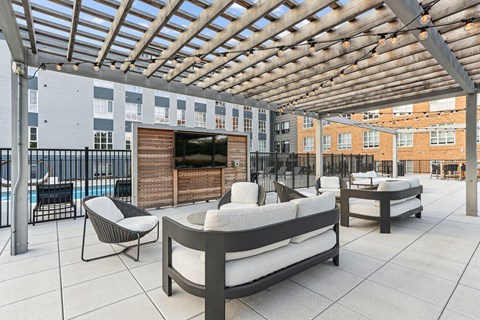 A patio with a couch, chairs, and a table under a wooden pergola.