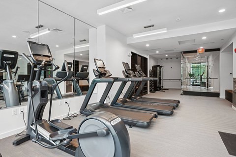 A spacious gym with treadmills, elliptical machines, and a mirrored wall.