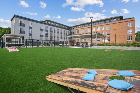 A playground with a wooden platform and blue cushions in the foreground and a building in the background.