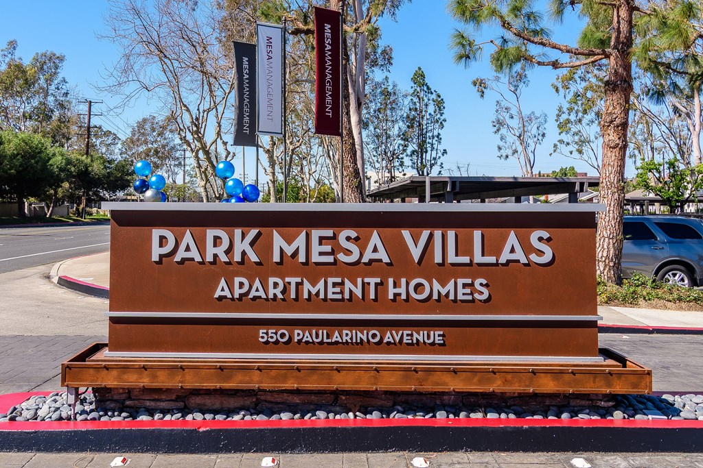 A brown sign for Park Mesa Villas Apartment Homes sits in front of a tree.