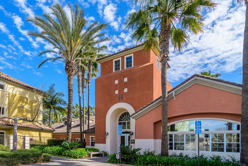 A building with a red brick tower and a white arched entrance is surrounded by palm trees.