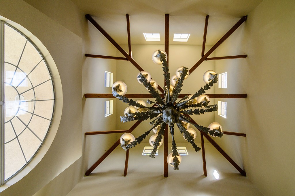 A chandelier with multiple lights hangs from the ceiling in a room with a large circular window.